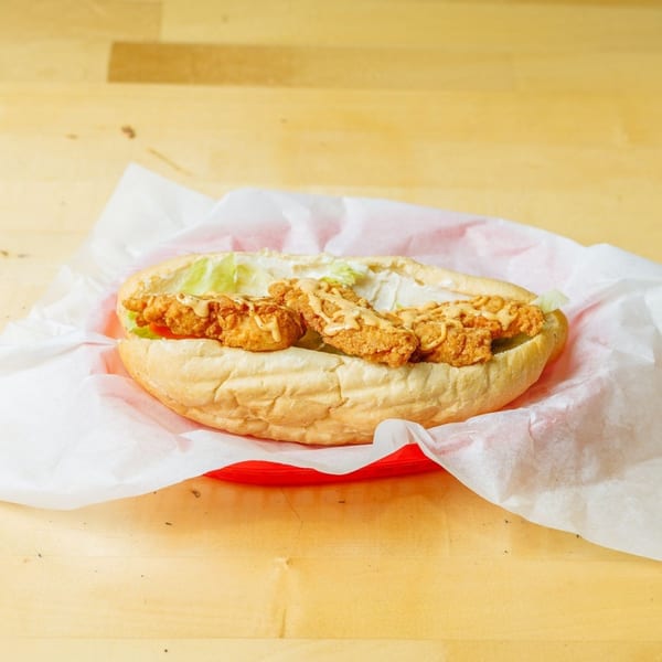Crispy fried chicken sandwich with lettuce and sauce, served in a red basket on a wooden table.