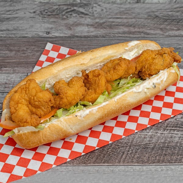 Crispy fried shrimp po'boy sandwich with lettuce, tomato, and mayonnaise on a red checkered paper.