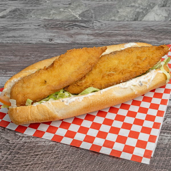 A fried fish po'boy sandwich with lettuce, tomato, and tartar sauce on a red and white checkered paper.