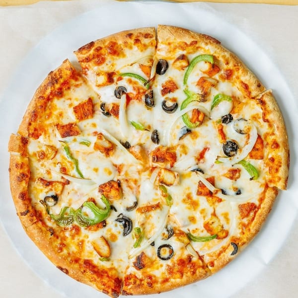 A whole pizza with chicken, green peppers, onions, and black olives on a white paper.