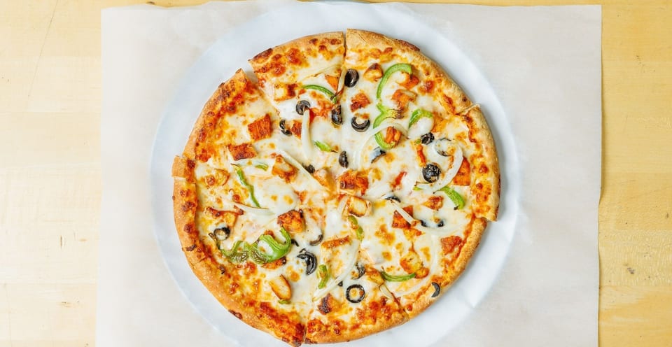 A whole pizza with chicken, green peppers, onions, and black olives on a white paper.