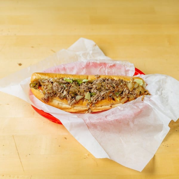 A large cheesesteak sandwich with steak, onions, and peppers in a red basket on a wooden table.