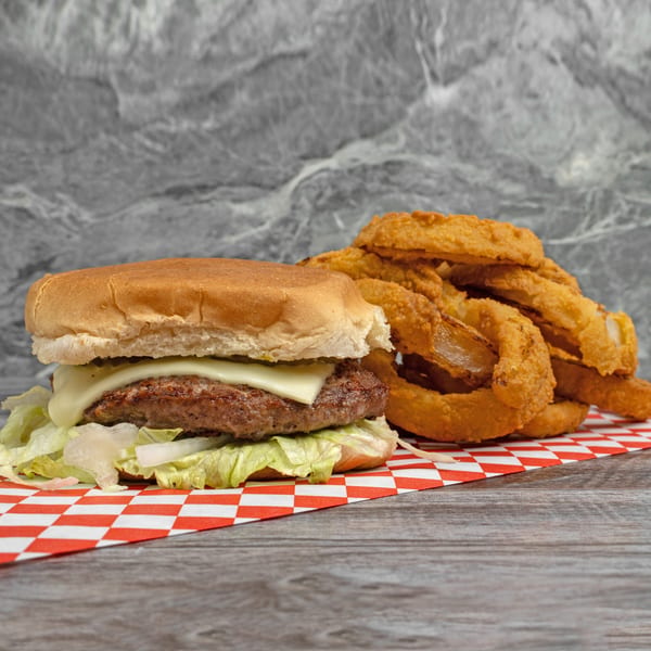 Cheeseburger with lettuce and onions, alongside a pile of golden onion rings on a checkered paper.