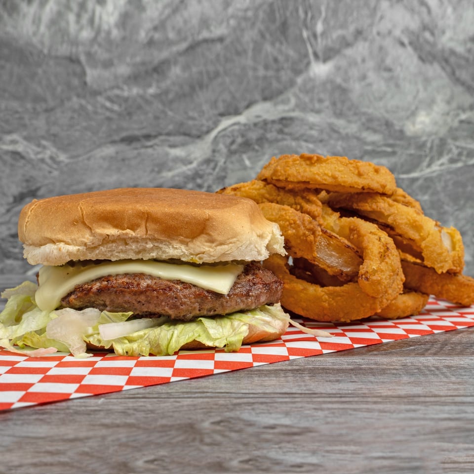 Cheeseburger with lettuce and onions, alongside a pile of golden onion rings on a checkered paper.