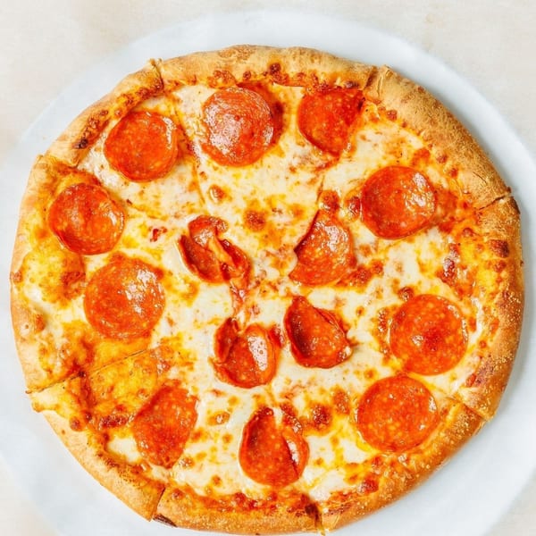 A whole pepperoni pizza, cut into slices, on a white plate and parchment paper.