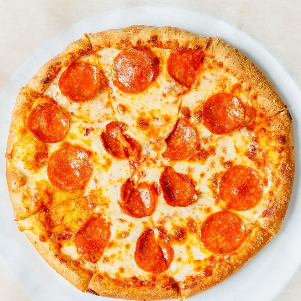A whole pepperoni pizza, cut into slices, on a white plate and parchment paper.