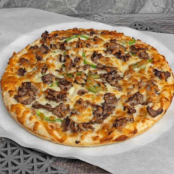 A whole round pizza with melted cheese, steak, and green peppers on a white paper liner.