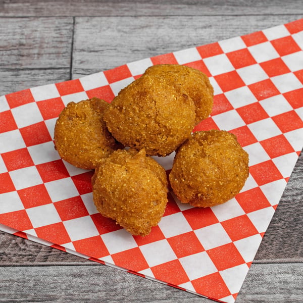 Five golden-brown hushpuppies rest on a red and white checkered paper on a wooden surface.